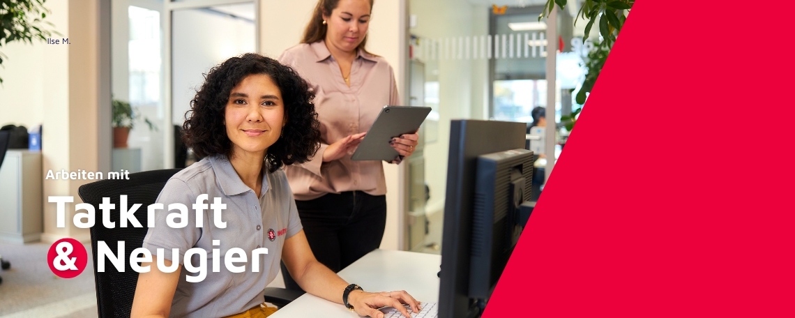 Zwei Frauen in einem modernen Büro: Eine sitzt am Schreibtisch und schaut freundlich in die Kamera, die andere steht dahinter mit einem Tablet in der Hand. Im Bild steht: ‚Arbeiten mit Tatkraft & Neugier‘.